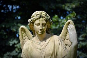 A close-up of a weathered stone angel statue, covered in some moss, with a serene expression and large wings