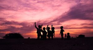 A silhouette of a group of children playing against a vibrant pink and orange sunset.