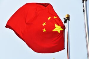 The Chinese flag waves against a bright blue sky, with its red background and golden stars representing unity and strength.