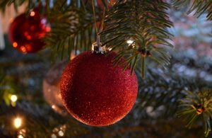 close-up shot of a Christmas tree branch shows a shimmering red glittery ornament hanging prominently