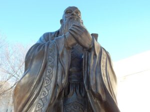 a large, bronze statue of Confucius, depicted with a long beard and traditional robes
