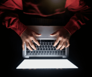 Hands type on a glowing laptop keyboard in a dark room.