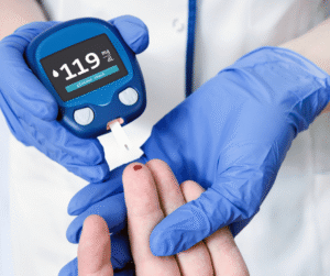 Gloved hands hold a glucometer displaying a reading of 119 mg/dL.