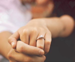 focus image of a man holding woman's hand wearing engagement ring