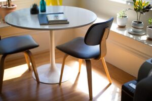 a modern dining setup with a white round table and two stylish chairs, bathed in natural light from a nearby window