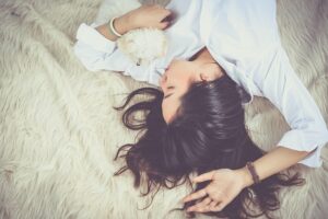 an overhead shot of a woman with long dark hair, wearing a white shirt, lying on a carpet