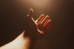 A person's open hand is extended upwards, illuminated by a warm, bright light from above