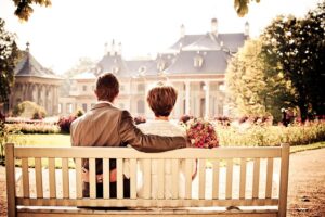 a couple, seen from behind, sitting on a white wooden bench in what appears to be a park