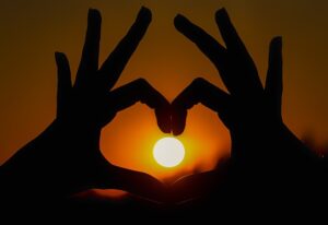 A silhouette of two hands forming a heart shape around the setting or rising sun