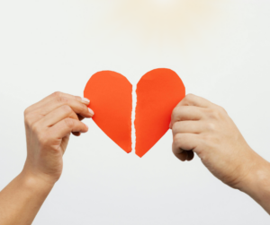 Hands holding two halves of a torn red paper heart