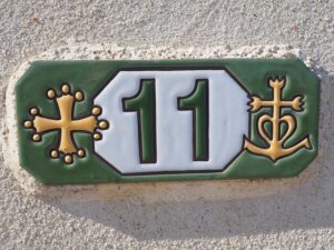 A decorative green tile with the house number 11 in the center, flanked by two religious crosses