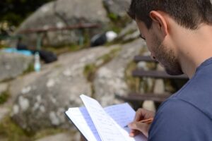 A man with a beard intently writing in a notebook with a pen