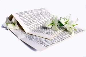 an open, handwritten letter on aged paper, laid flat on a white surface. White bougainvillea flowers with green leaves are placed on top of the letter