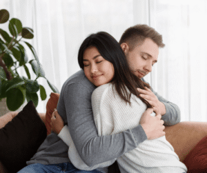 A young couple sharing a tender, affectionate hug with their eyes closed.