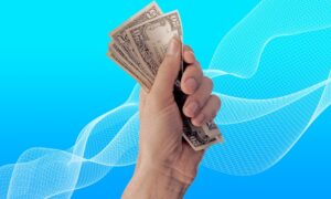 a hand holding several US dollar bills against a blue background