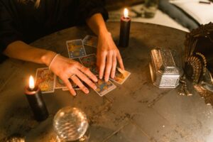 Two hands reach for tarot cards on a round table, lit by the glow of two candles.