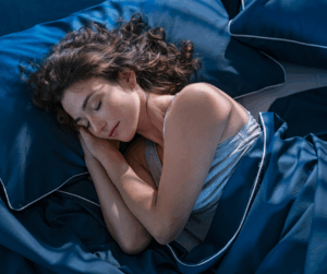 A woman with curly brown hair sleeps soundly in a dark blue bed.