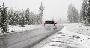 a white SUV driving away on a wet, snow-dusted asphalt road