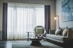 Modern living room with large windows, grey sofa and armchair, and round coffee table