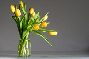 a clear glass vase holding a bouquet of vibrant yellow tulips with bright green stems and leaves