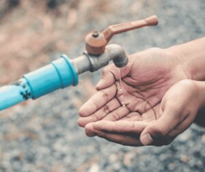 Hands cupped beneath an outdoor spigot catching drops of dripping water.