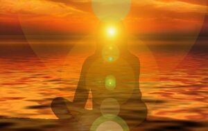 A silhouette of a person meditating in front of a sunset over the ocean, with glowing circles of light