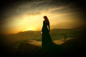woman standing on top of hill facing the sunrise