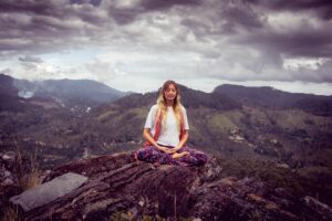 a person sitting in a meditation pose on a large rock outcropping high on a mountaintop