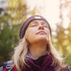 lose-up shot of a woman with her eyes closed and head tilted slightly upwards, wearing a beanie and outdoor gear