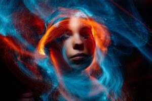 a woman's face illuminated by swirling light trails in vibrant blue and orange